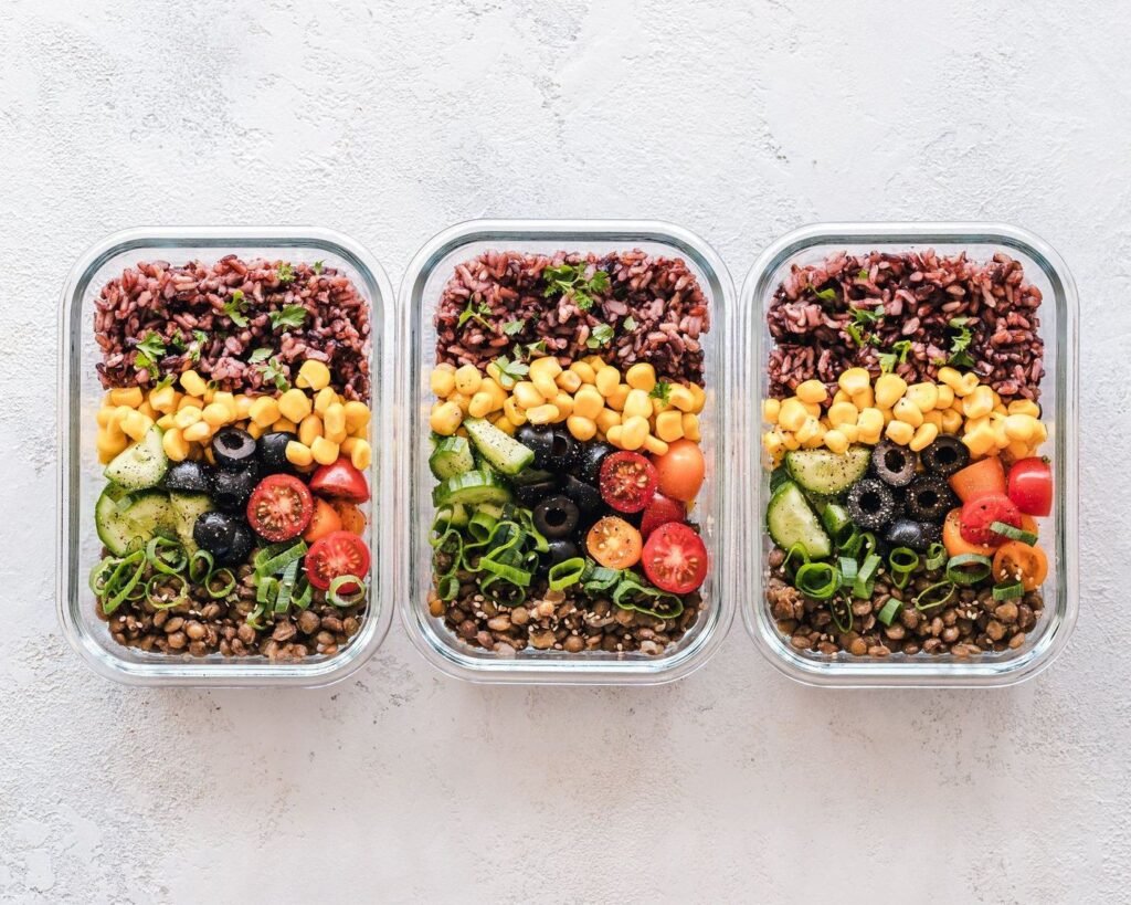 Glass meal prep containers with rice, lentils and fresh vegetables